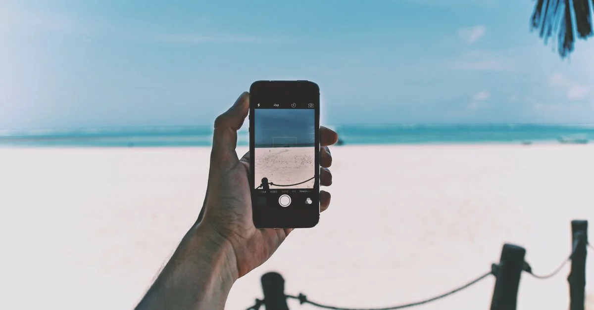 Une main tenant un smartphone capturant une vue de plage pittoresque.