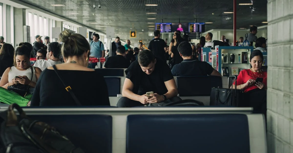 Voyageurs assis et attendant dans le terminal de l'aéroport de São Paulo, utilisant des smartphones.
