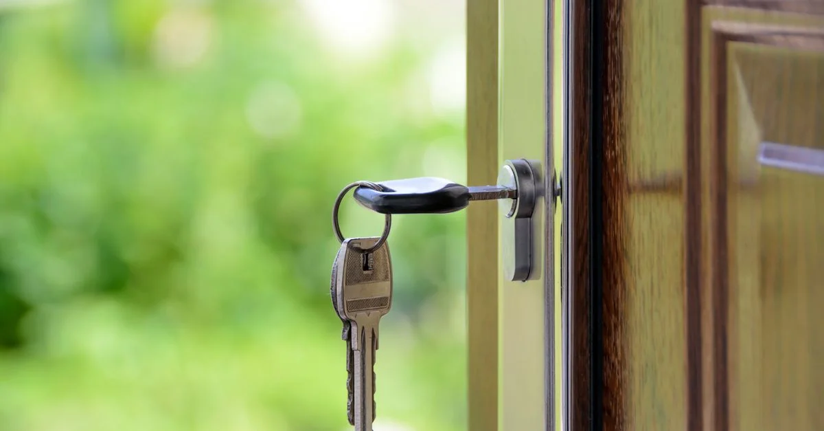 Clé insérée dans une serrure de porte sur fond vert flou, symbolisant la sécurité et l'immobilier.