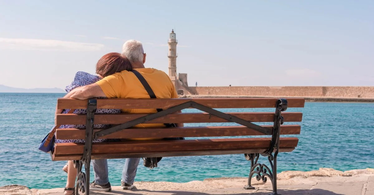 Un couple âgé profite d'un moment paisible au bord de la mer, assis sur un banc avec un phare en vue.