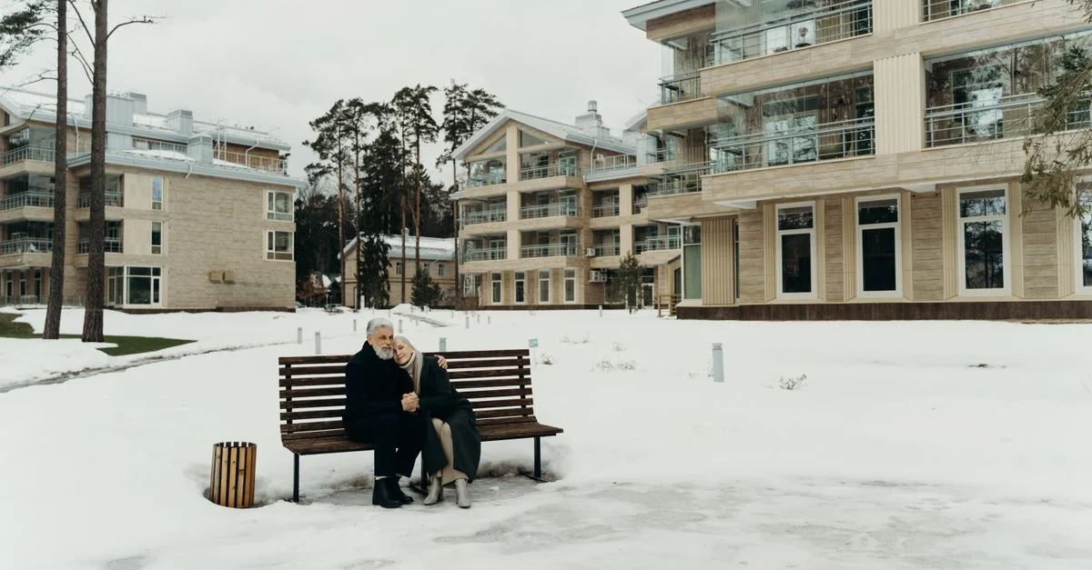 Un couple senior assis sur un banc au milieu d'appartements modernes couverts de neige.