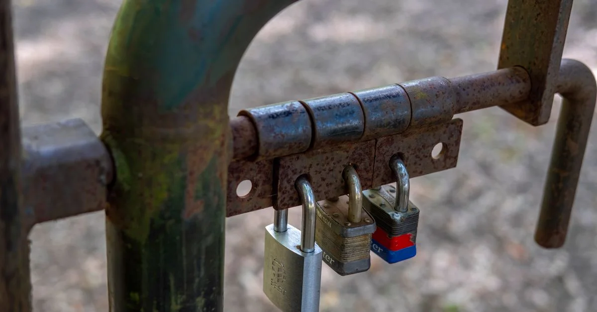 Gros plan sur une porte rouillée sécurisée par trois cadenas, symbolisant la sécurité et la protection.