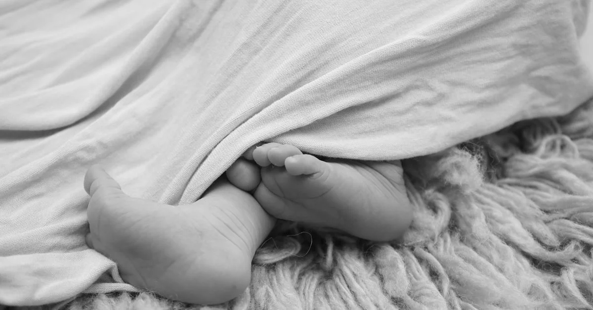 Photo en noir et blanc de pieds de bébé sous une douce couverture sur un tapis en laine.