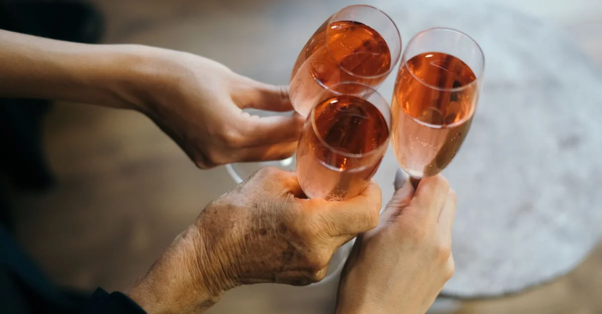 Trois mains tenant et s'entrechoquant des flûtes de champagne rosé lors d'un toast de célébration.