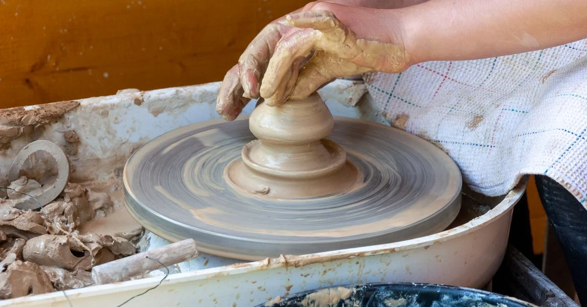 Gros plan sur des mains façonnant de l'argile sur un tour de potier, illustrant des techniques artisanales traditionnelles.