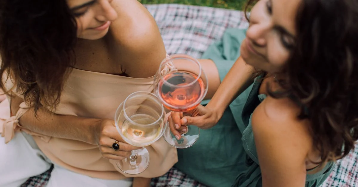 Deux femmes profitant d'un rassemblement décontracté en plein air tout en levant leur verre de vin.