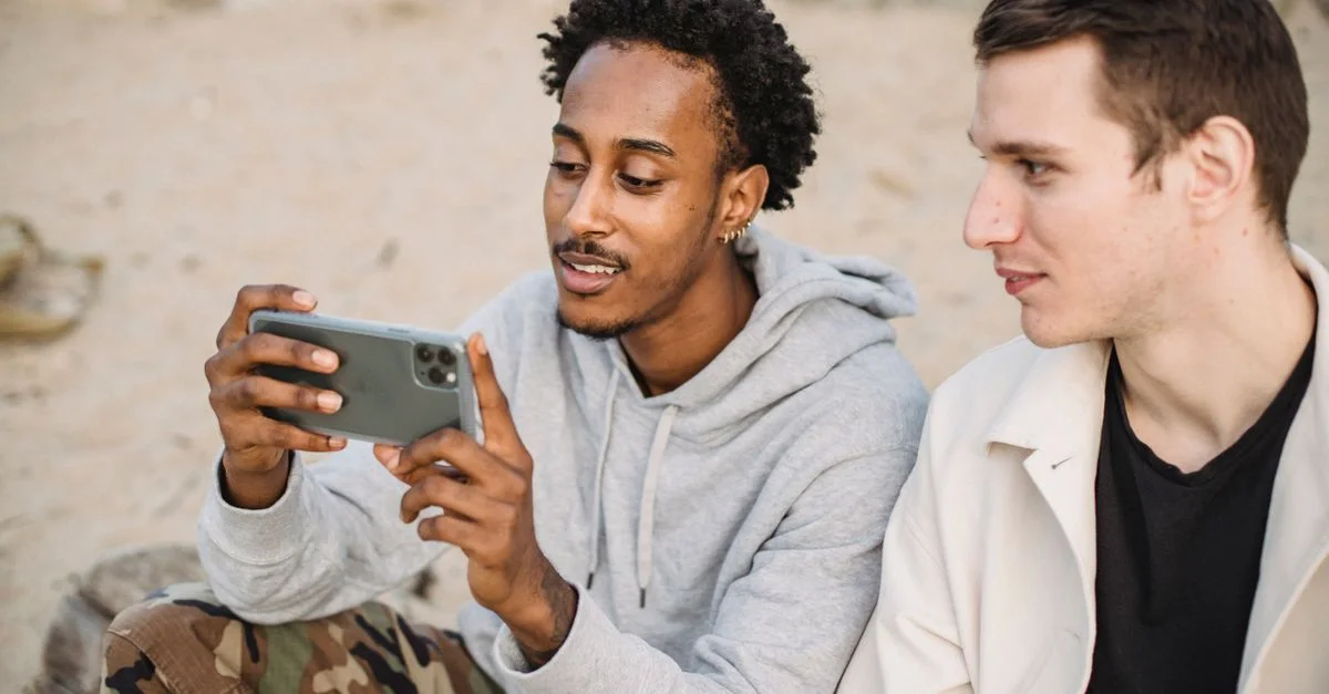 Deux jeunes hommes assis sur la plage partageant et naviguant ensemble sur un smartphone.