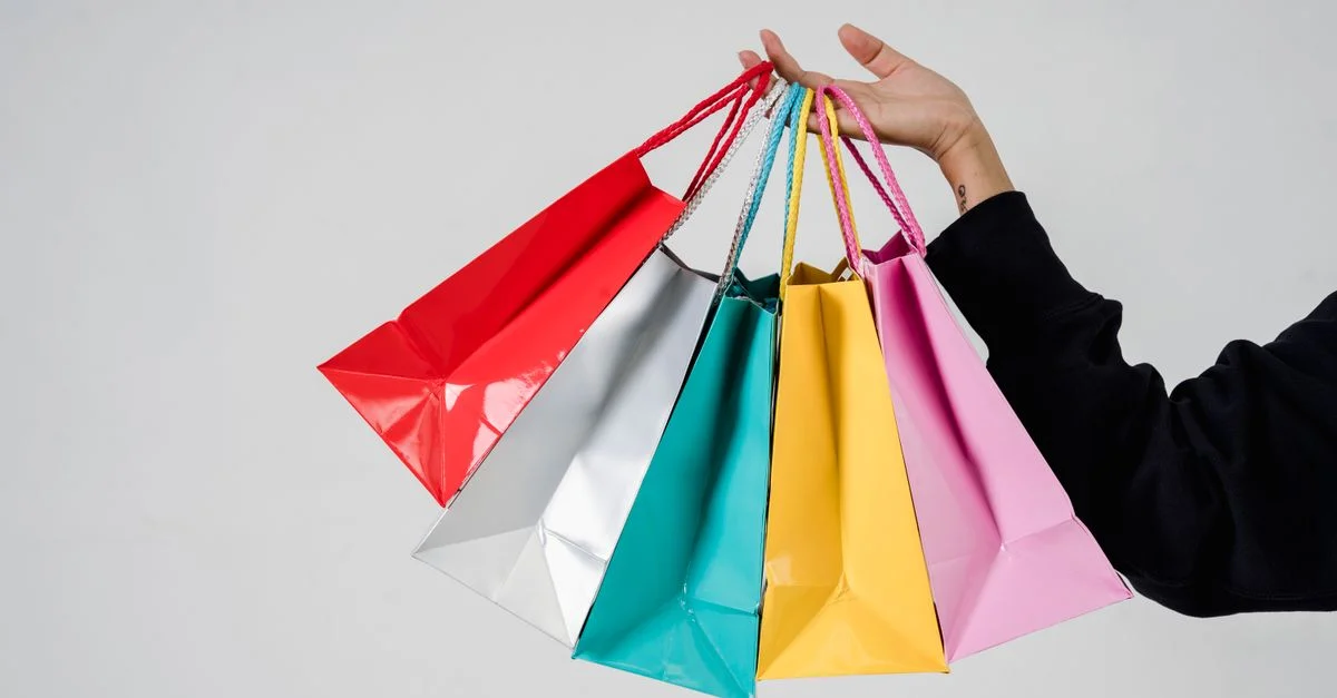 Gros plan de sacs de shopping colorés tenus dans une main sur un fond gris.
