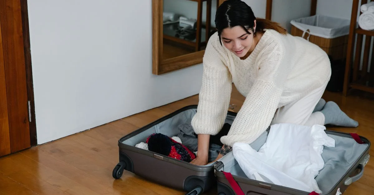 Une femme est à genoux sur le sol en train de ranger des vêtements dans une valise dans une chambre confortable.